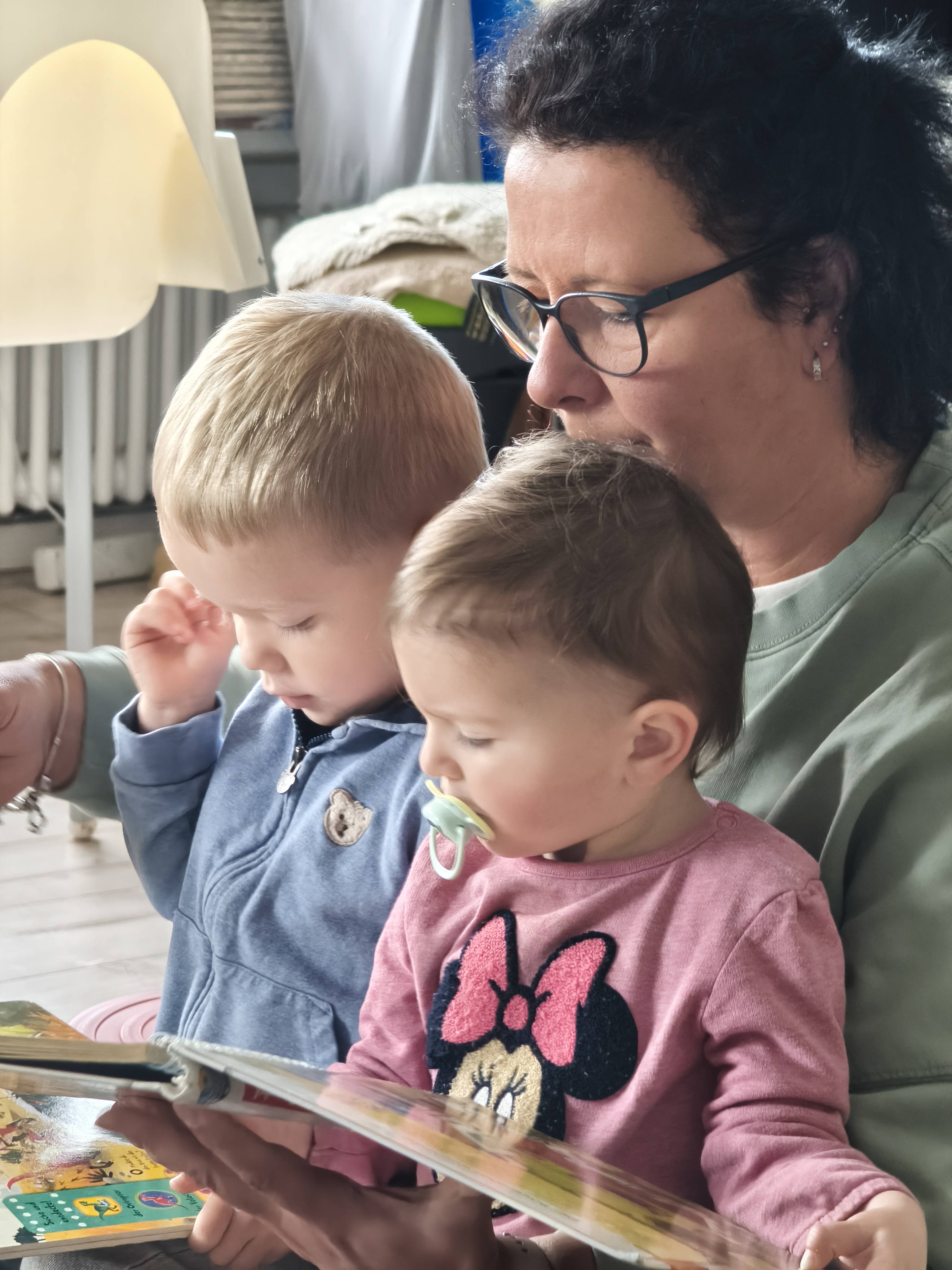 Die Tagesmutter liest zwei Kleinkindern aus einem Bilderbuch vor