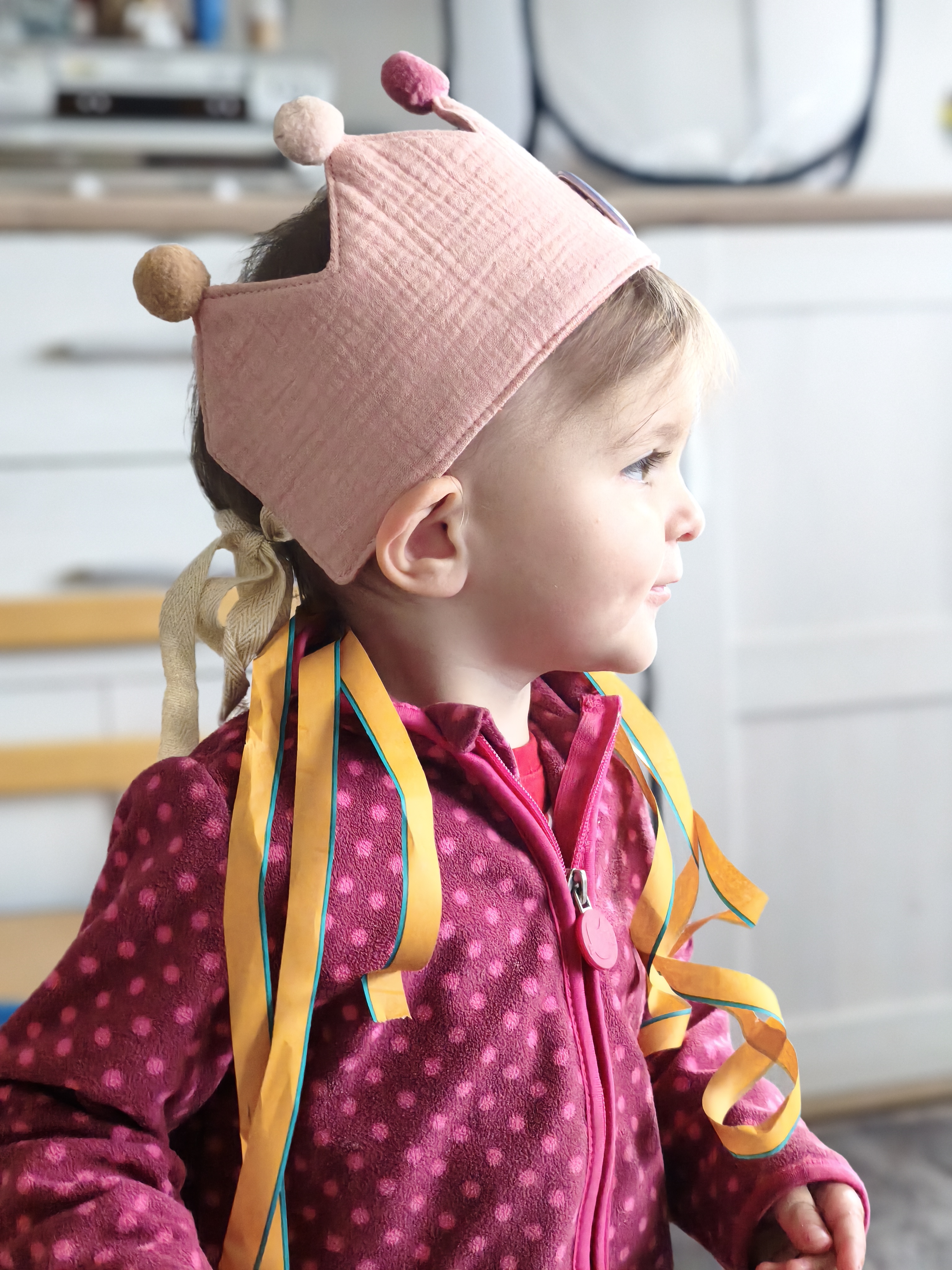 Ein Kind trägt eine rosafarbene Geburtstagskrone mit bunten Bändern